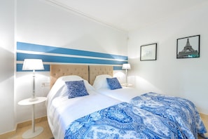 Habitación de hotel con una cama, dos lámparas de noche, un cabecero y dos cuadros en la pared.