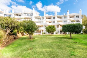 Un immeuble blanc à plusieurs étages, doté de balcons, entouré de pelouses et d’arbres bien entretenus.