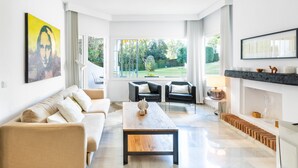 Una sala de estar moderna con un sofá, una mesa de centro y dos sillones. Hay una chimenea con repisa y un ventanal grande que ofrece vistas al jardín.