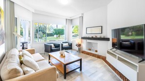 Una sala de estar moderna con un sofá, una mesa de centro, chimenea, televisor y ventanas amplias.