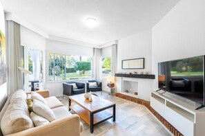A modern living room with a sofa, coffee table, fireplace, TV, and large windows.