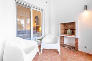 A room with a sliding glass door, a white chair, a small table, and a brick fireplace.