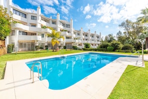 A swimming pool surrounded by a well-maintained lawn and a multi-story building with balconies.