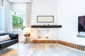 A modern living room with a fireplace, a black leather sofa, a side table with a lamp, and a TV mounted on the wall.