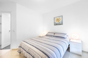 A bedroom with a bed, nightstands, a wall-mounted painting, and a door.