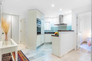 A modern kitchen with white cabinetry, a built-in oven, and a stainless steel range hood.