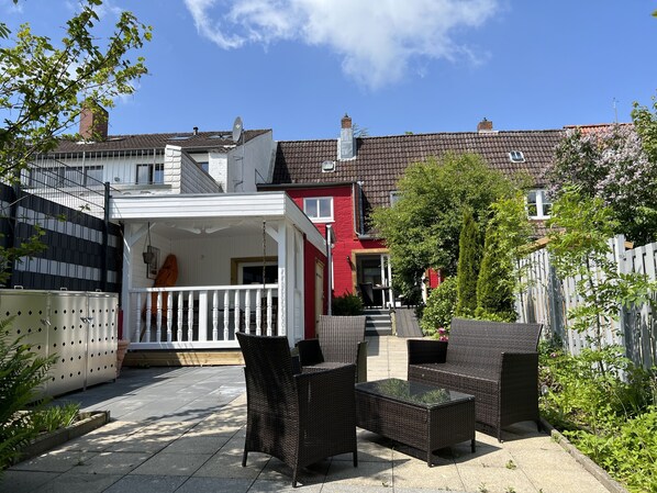 A courtyard with outdoor furniture, a white building with a balcony, and a red house in the background. - Beautiful vacation home directly on the canal (Friedrichstadt)