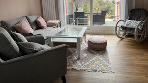 A living room with a grey sofa, a glass coffee table, a patterned rug, and a wheelchair-accessible chair. - Beautiful vacation home directly on the canal (Friedrichstadt)