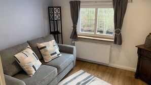 A cozy living room with a grey sofa, patterned cushions, a striped rug, a radiator, and a window with curtains. - Beautiful vacation home directly on the canal (Friedrichstadt)