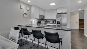 Una cocina moderna con una isla central, taburetes de bar y un microondas.