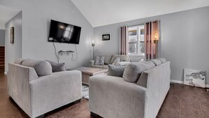 Una sala de estar moderna con sofás grises, un televisor de pantalla plana y una ventana con cortinas.