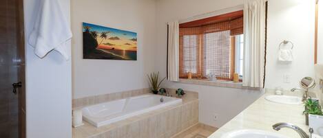 Ein Badezimmer mit Badewanne, Waschbecken, einem Fenster mit Jalousien, einem Handtuch an der Wand und einem Sonnenuntergangsbild.