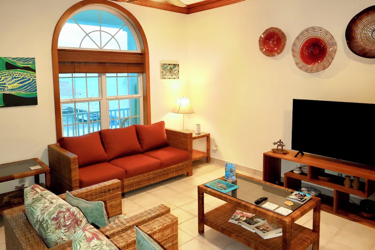 Ein Wohnzimmer mit großem Fenster, Deckenventilator, Sofa, Couchtisch und Fernseher.