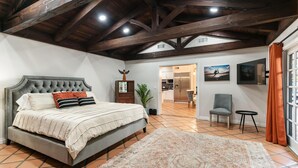 Une chambre avec un grand lit, un plafond en bois, une télévision et une vue sur la cuisine.