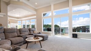 Een ruime woonkamer met een grote hoekbank, een ronde salontafel en uitzicht op een balkon met buitenmeubilair.