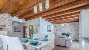 A modern dining area with white chairs, a wooden ceiling, and a stone wall. - Stone Villa Gelosia Rustica with heated pool (Sukošan)