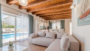 A modern living room with a beige sofa, a glass coffee table, and wooden beams on the ceiling. - Stone Villa Gelosia Rustica with heated pool (Sukošan)