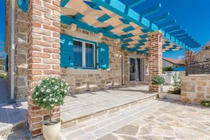 A stone building with a covered patio, blue shutters, and potted plants. - Stone Villa Gelosia Rustica with heated pool (Sukošan)