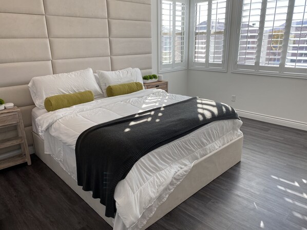 Relax in a serene bedroom with a large bed, grey headboard, and wooden nightstand.