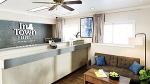 A hotel reception area with a counter, a sofa, a coffee table, and a ceiling fan.