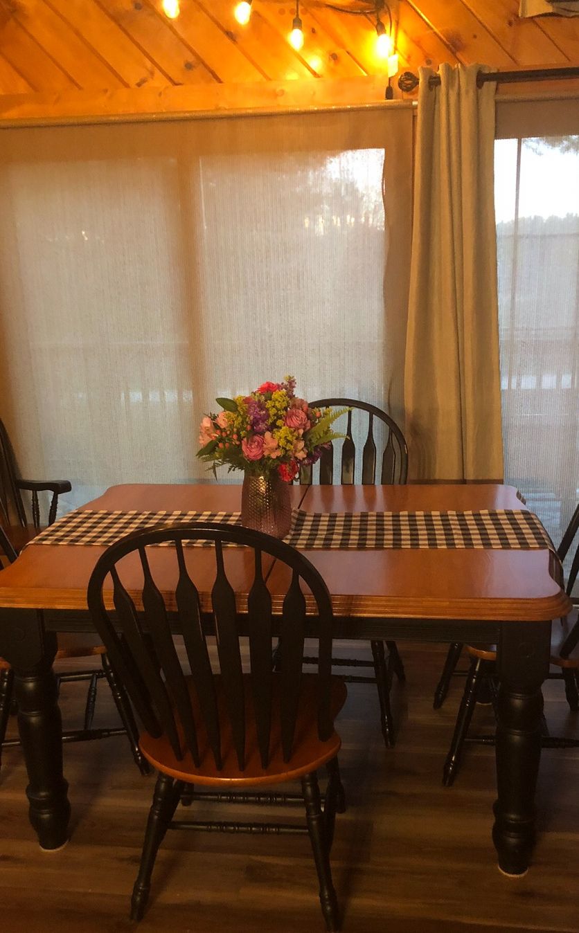 A wooden dining table with a checkered placemat, surrounded by four chairs with a unique back design. A vase with flowers is placed on the table.