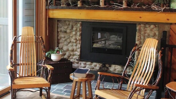 Une pièce chaleureuse avec une cheminée en pierre, deux fauteuils en osier, une petite table et un téléviseur fixé au-dessus de la cheminée.