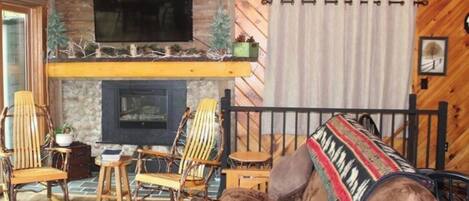 A cozy cabin interior with a stone fireplace, wooden walls, and a comfortable seating area with chairs and a sofa.