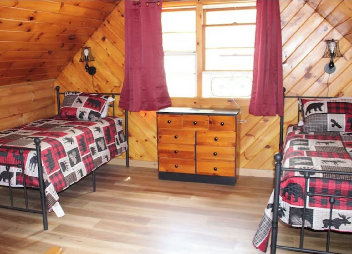 Une chambre confortable avec deux lits, une commode en bois et une fenêtre avec des rideaux.