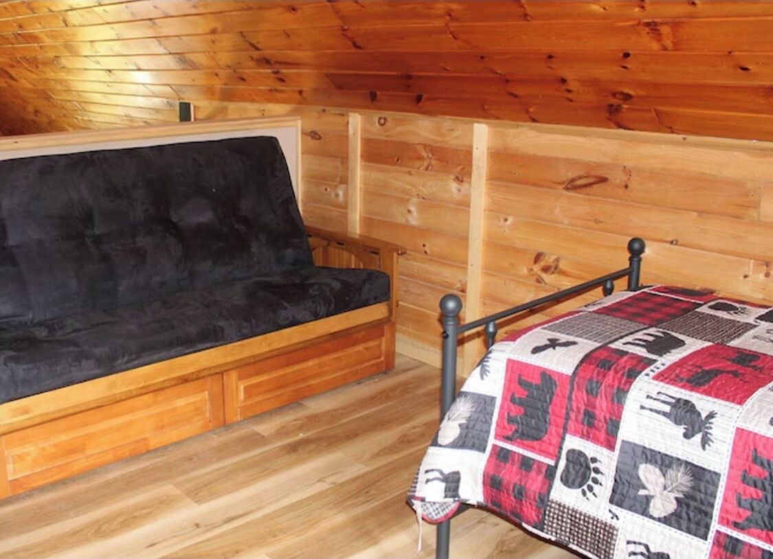 A wooden cabin interior with a black sofa and a metal bed frame.