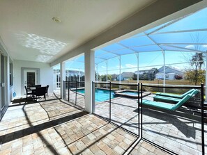 A covered patio with a pool, outdoor furniture, and a view of neighboring houses.