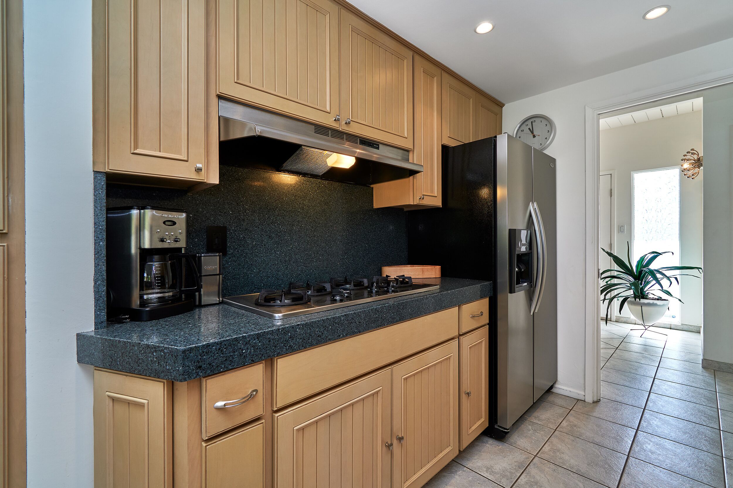 A modern kitchen with wooden cabinets, a stainless steel refrigerator, and a built-in gas stove.