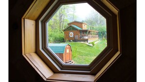 Vista attraverso una finestra ottagonale di una casa con tetto verde, un patio in legno e un prato curato.