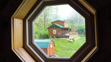 A view through an octagonal window of a house with a green roof, a wooden deck, and a well-maintained lawn.