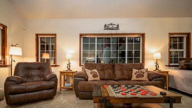 A cozy living room with a leather armchair, a sofa with paw print cushions, and a checkered coffee table. - Hikers paradise w/ saltwater hot tub (Port Angeles)