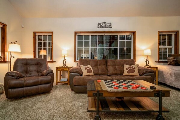 A cozy living room with a leather armchair, a sofa with paw print cushions, and a checkered coffee table. - Hikers paradise w/ saltwater hot tub (Port Angeles)
