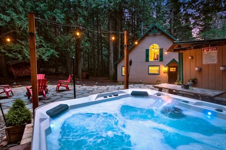 A hot tub in a forested area with a wooden building and a sign labeled 'SPA RULES'.