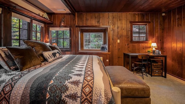 A cozy log cabin bedroom with a large bed, a desk, and a window overlooking the forest. - Hikers paradise w/ saltwater hot tub (Port Angeles)