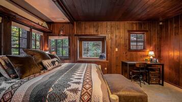 A cozy log cabin bedroom with a large bed, a desk, and a window overlooking the forest.