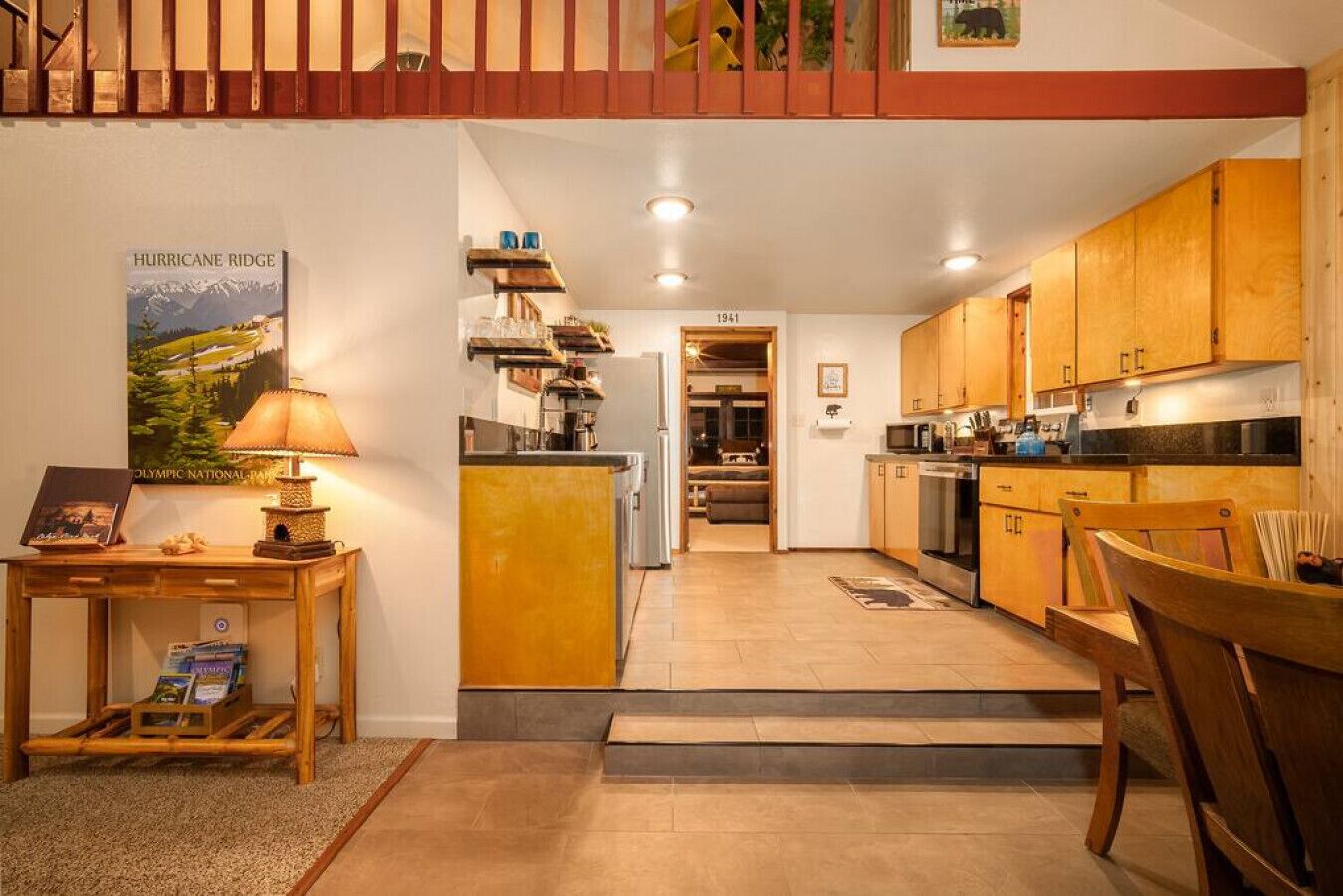 A compact kitchen with wooden cabinets, a dining area with a table and chairs, and a staircase leading to an upper level.