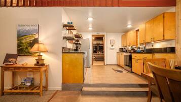 A compact kitchen with wooden cabinets, a dining area with a table and chairs, and a staircase leading to an upper level.