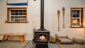 A cozy living room with a wood-burning stove, a wooden table, a cushioned bench, and two windows. - Hikers paradise w/ saltwater hot tub (Port Angeles)