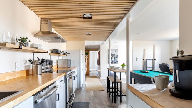 A modern kitchen with stainless steel appliances, wooden countertops, and a pool table in the adjacent room.