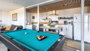 A pool table in a modern living area with a kitchen in the background.