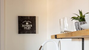 A kitchen with a wooden countertop, a sink, a faucet, and a shelf with glasses and a plant.