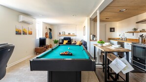 A pool table in a modern living room with a kitchen area and a dining table.