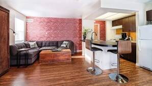 Une cuisine moderne avec un mur d’accent en briques, un coin bar et un salon doté d’un canapé d’angle.