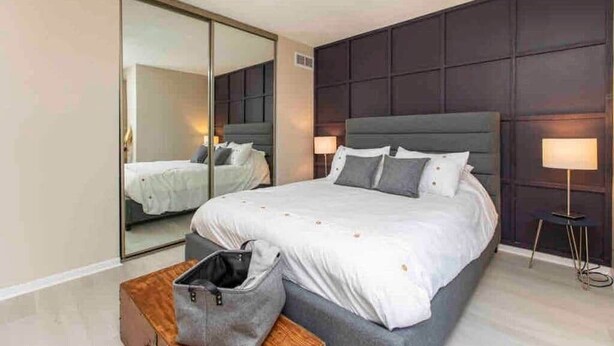 Une chambre d’hôtel moderne avec un grand lit, un miroir, une table de chevet et une lampe.