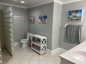 A bathroom with a toilet, a vanity with a mirror, a shower area, and a sink. There are framed pictures on the wall and a towel hanging on the wall. - Crystal Conch sleeps 16, private home close to beach access (Emerald Isle)