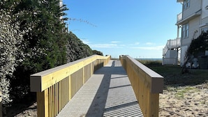 A wooden boardwalk leading to a beach, flanked by dense foliage and buildings. - Crystal Conch sleeps 16, private home close to beach access (Emerald Isle)