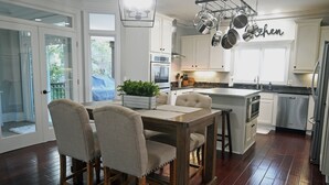 A kitchen with white cabinets, a dining table with chairs, and hanging pots. - Crystal Conch sleeps 16, private home close to beach access (Emerald Isle)